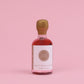 Bottle of whisky infused maple syrup with a gold cap on a pink background