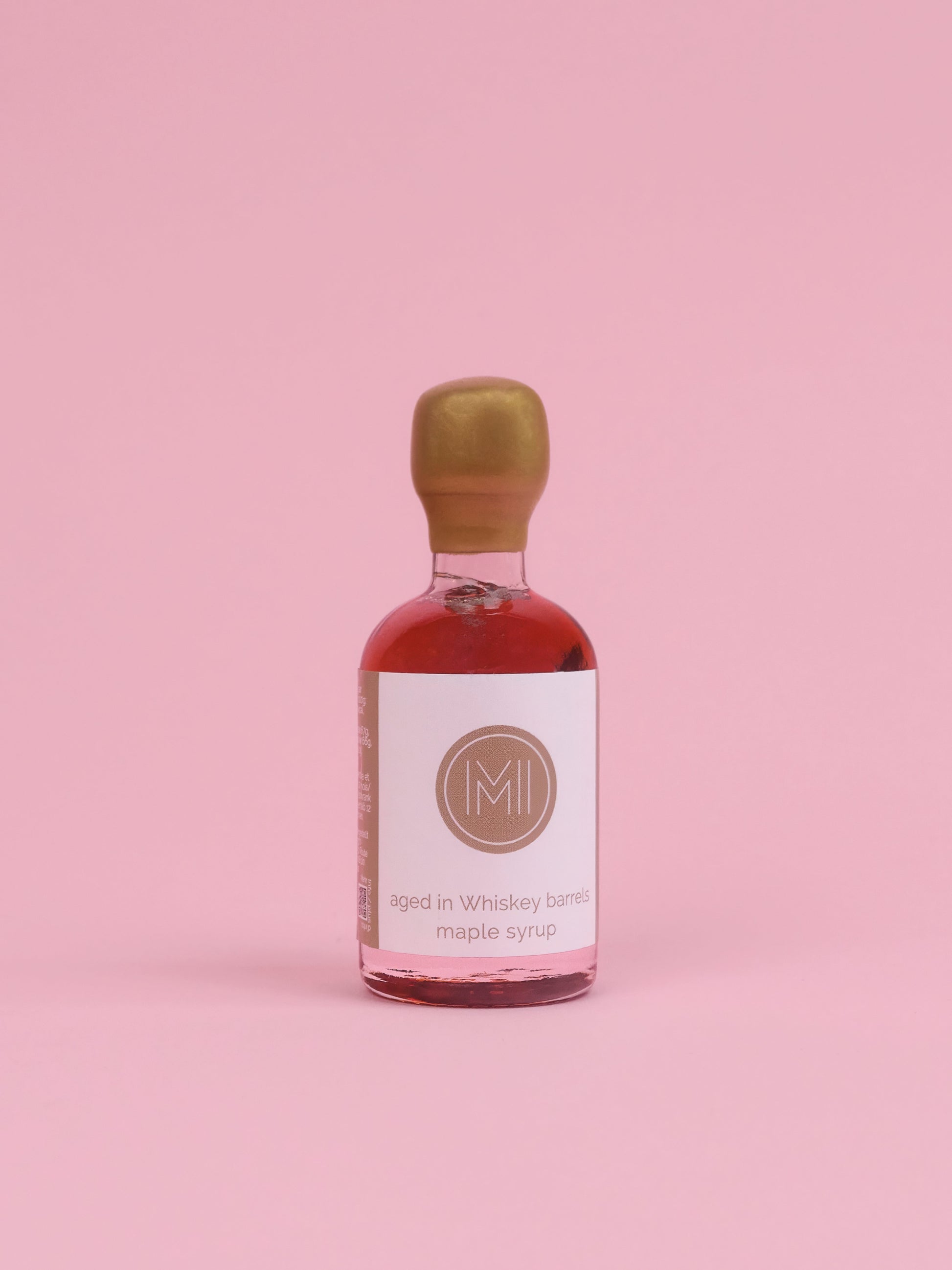 Bottle of whisky infused maple syrup with a gold cap on a pink background