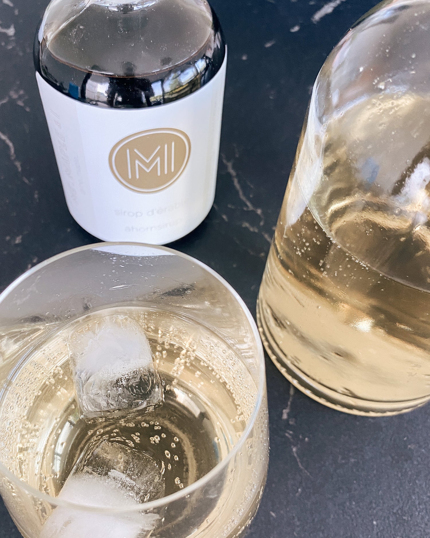 a glass, a glass bottle and a glass bottle with maple syrup on a grey countertop